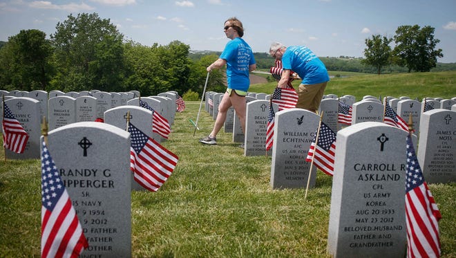 Lerynne West of West Des Moines and Tom Clingan, also of West Des Moines, place flags at the grave markers at the Iowa Veterans Cemetery in Adel on Friday, May 25, 2018.